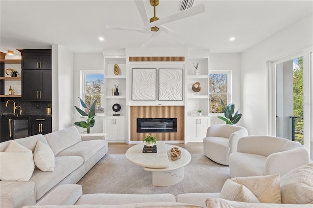 living room featuring visible vents, a glass covered fireplace, wine cooler, light wood-type flooring, and recessed lighting