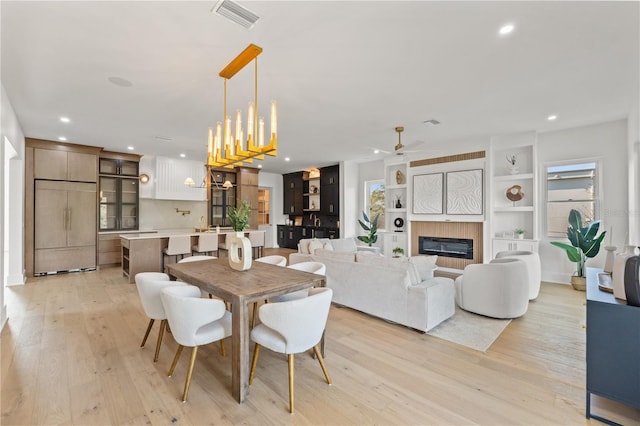 dining room with built in shelves, light wood finished floors, recessed lighting, visible vents, and a tile fireplace