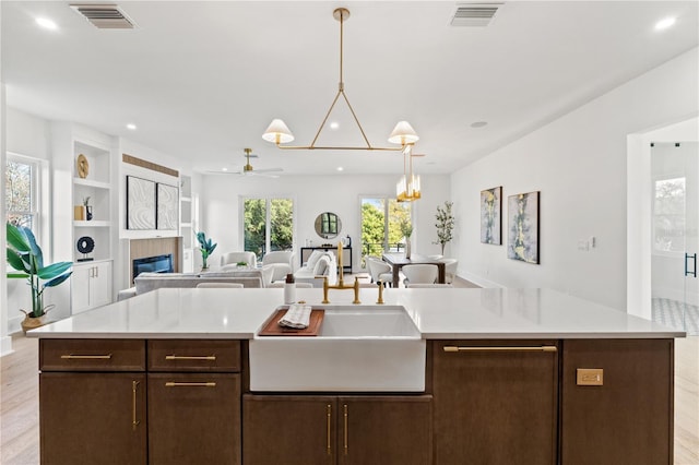 kitchen featuring dark brown cabinetry, visible vents, open floor plan, and a sink