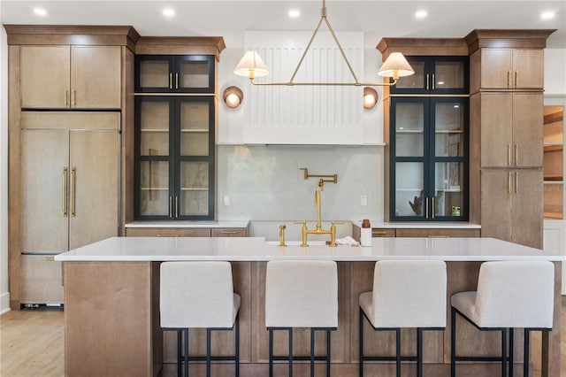 kitchen with glass insert cabinets, light countertops, paneled fridge, and light wood finished floors