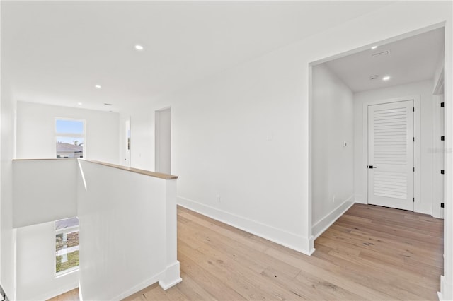 hallway featuring light wood-type flooring, baseboards, an upstairs landing, and recessed lighting