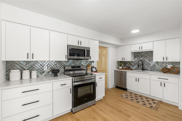 kitchen featuring sink, white cabinetry, tasteful backsplash, light hardwood / wood-style flooring, and appliances with stainless steel finishes