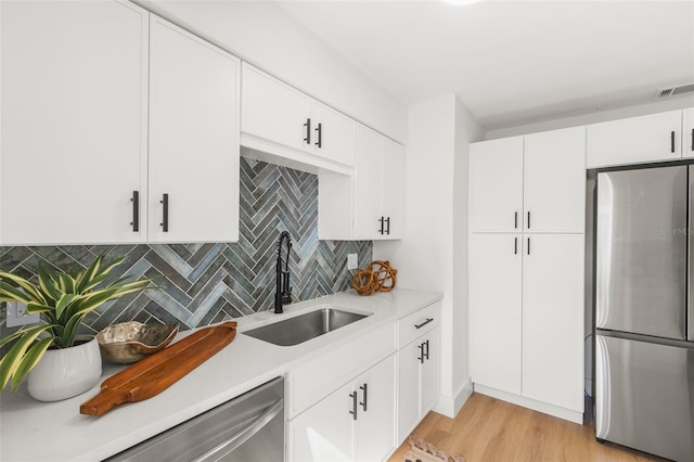 kitchen with sink, appliances with stainless steel finishes, white cabinets, decorative backsplash, and light wood-type flooring