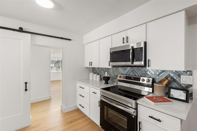 kitchen featuring white cabinetry, backsplash, stainless steel appliances, a barn door, and light wood-type flooring