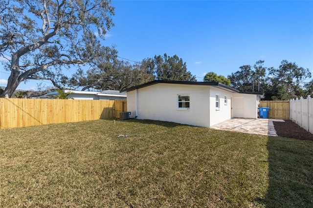 rear view of property featuring central AC unit, a lawn, and a patio