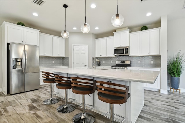 kitchen with a kitchen bar, white cabinetry, decorative light fixtures, appliances with stainless steel finishes, and a kitchen island with sink