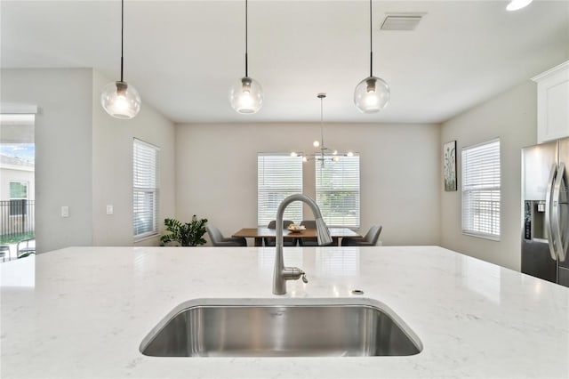 kitchen featuring hanging light fixtures, sink, stainless steel fridge, and light stone counters