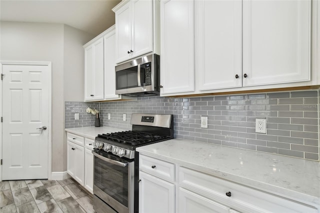 kitchen with white cabinetry, stainless steel appliances, light stone countertops, and backsplash