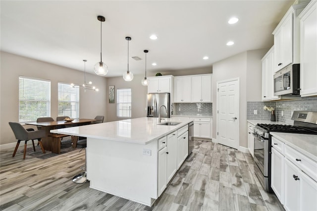 kitchen with sink, white cabinetry, hanging light fixtures, appliances with stainless steel finishes, and an island with sink