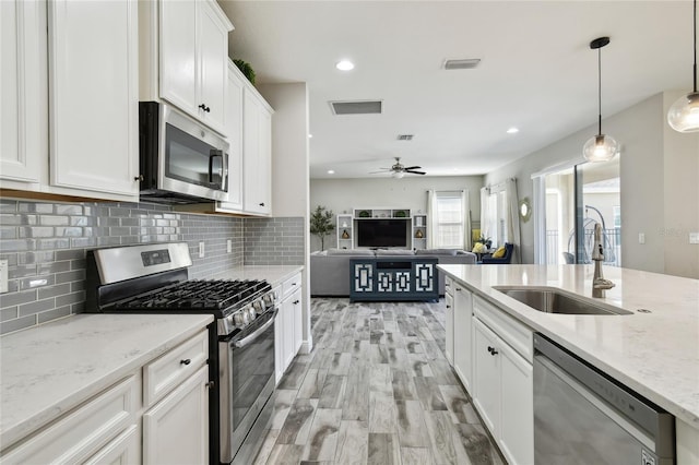 kitchen featuring sink, light stone counters, appliances with stainless steel finishes, pendant lighting, and white cabinets