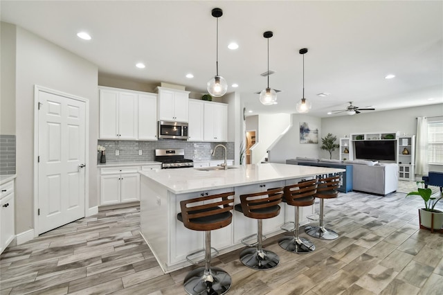 kitchen with stainless steel appliances, a kitchen island with sink, sink, and white cabinets