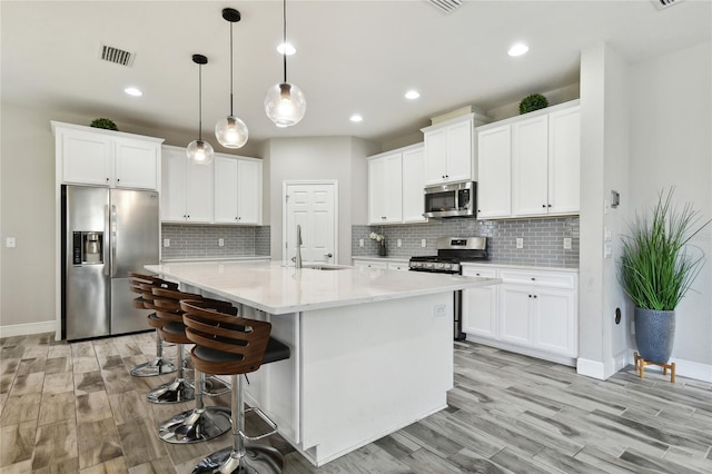 kitchen with decorative light fixtures, sink, white cabinets, a kitchen island with sink, and stainless steel appliances