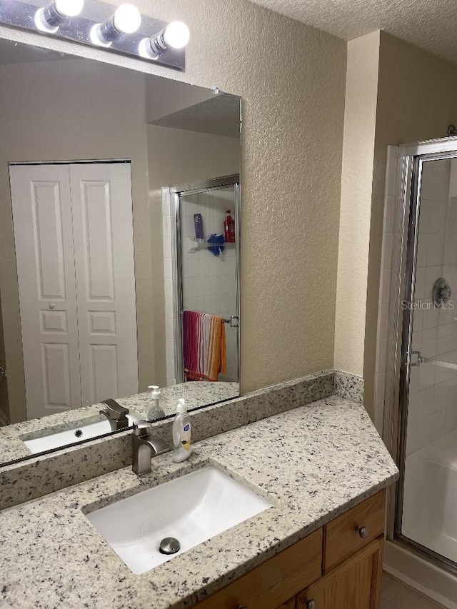 bathroom featuring vanity, a shower with shower door, and a textured ceiling