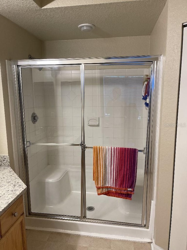 bathroom featuring vanity, tile patterned floors, a shower with door, and a textured ceiling