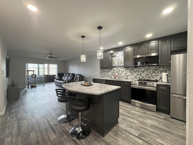 kitchen with a kitchen island, pendant lighting, a kitchen bar, decorative backsplash, and stainless steel appliances