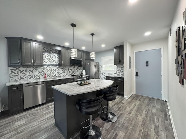 kitchen featuring a breakfast bar area, hanging light fixtures, stainless steel appliances, a kitchen island, and light wood-type flooring