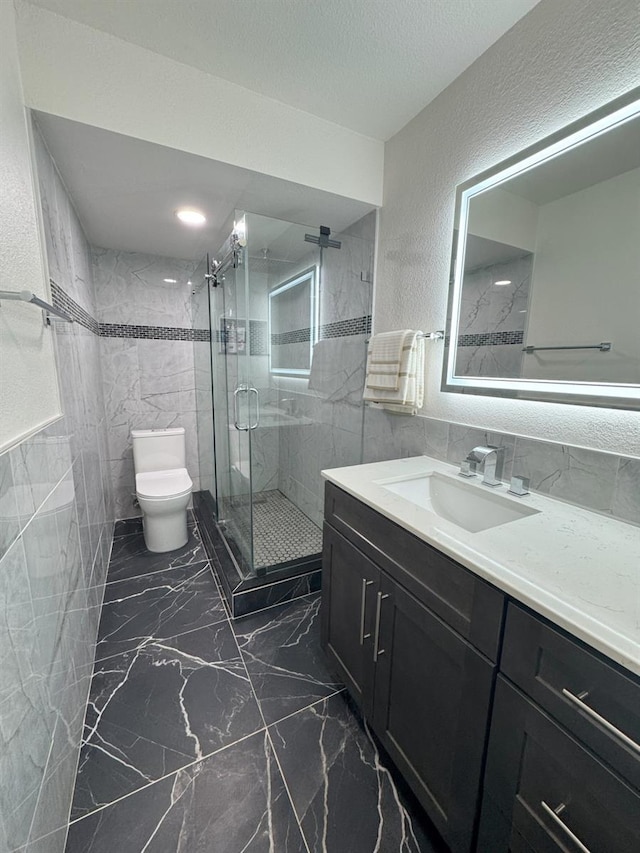 bathroom featuring toilet, a shower with shower door, tile walls, a textured ceiling, and vanity