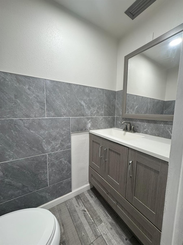 bathroom with hardwood / wood-style flooring, vanity, toilet, and tile walls