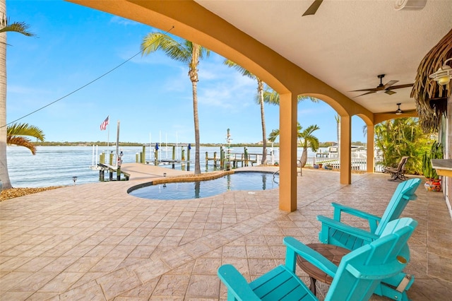 view of swimming pool featuring a patio area, a boat dock, ceiling fan, and a water view