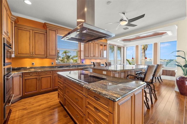 kitchen with dark stone countertops, a kitchen breakfast bar, island exhaust hood, a center island, and black electric cooktop