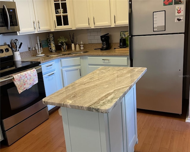 kitchen with sink, white cabinets, stainless steel appliances, light stone countertops, and light hardwood / wood-style flooring