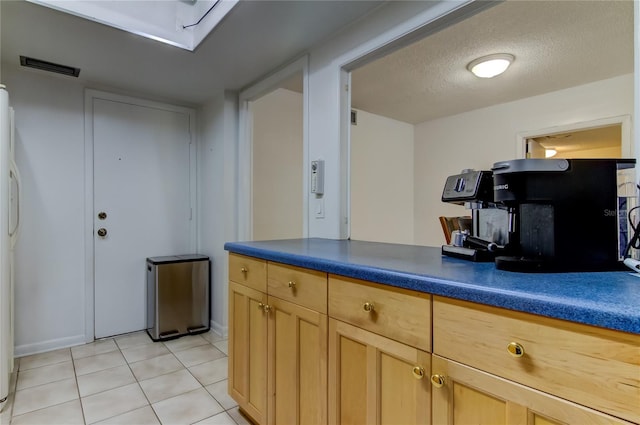 5396 Gulf Blvd Unit 110, St Pete Beach, FL 33706 - kitchen with light tile patterned flooring, light brown cabinetry, dark countertops, a textured ceiling, and baseboards