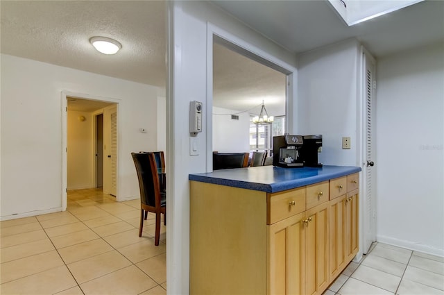 5396 Gulf Blvd Unit 110, St Pete Beach, FL 33706 - kitchen featuring light tile patterned flooring, dark countertops, light brown cabinets, a chandelier, and baseboards