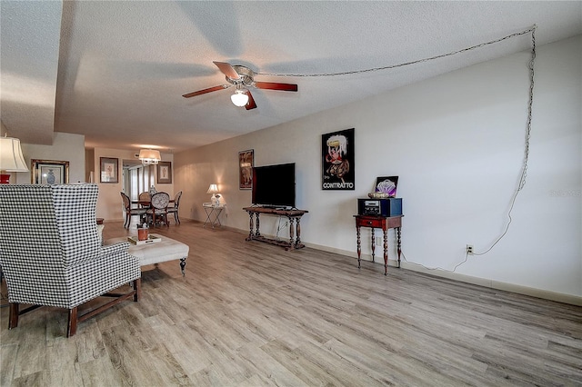 living room featuring a ceiling fan, baseboards, a textured ceiling, and light wood finished floors