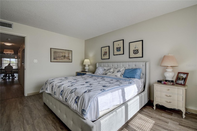 bedroom with a textured ceiling, wood finished floors, visible vents, and baseboards