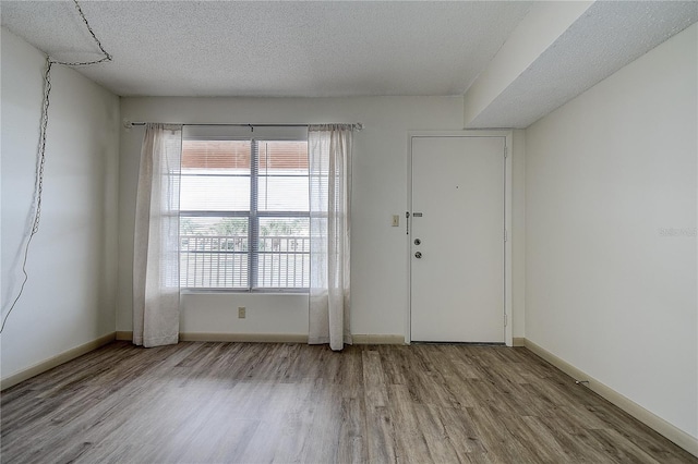 empty room with a textured ceiling, baseboards, and light wood-style floors
