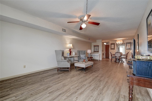 sitting room featuring visible vents, light wood-style flooring, a ceiling fan, a textured ceiling, and baseboards