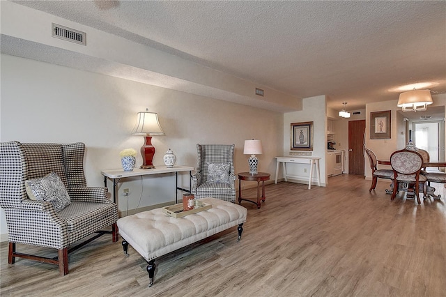 living area featuring a textured ceiling, light wood-style flooring, and visible vents