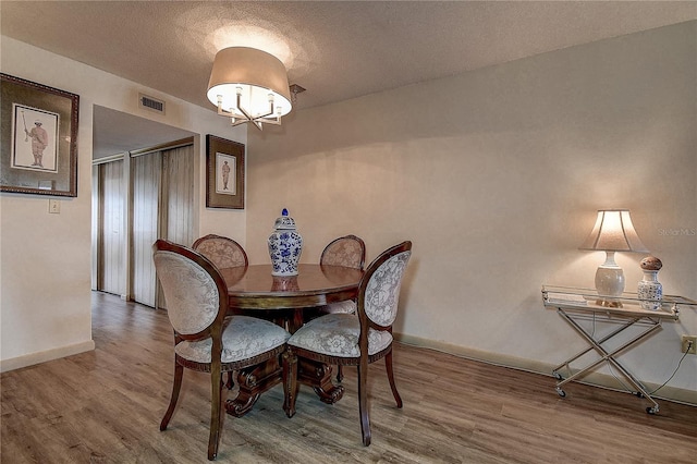 dining area with visible vents, an inviting chandelier, a textured ceiling, wood finished floors, and baseboards