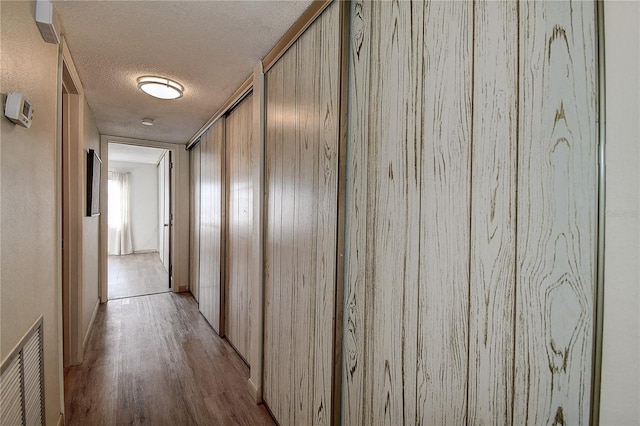 hall featuring light wood-style flooring, visible vents, and a textured ceiling