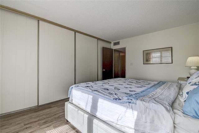 bedroom featuring a textured ceiling, a closet, wood finished floors, and visible vents