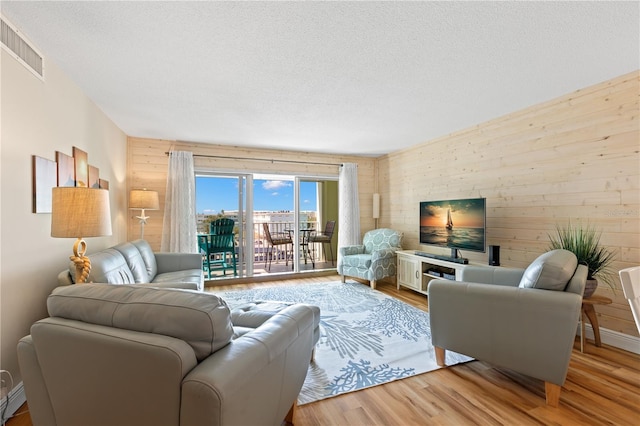 living room with a textured ceiling, light wood-type flooring, and wood walls