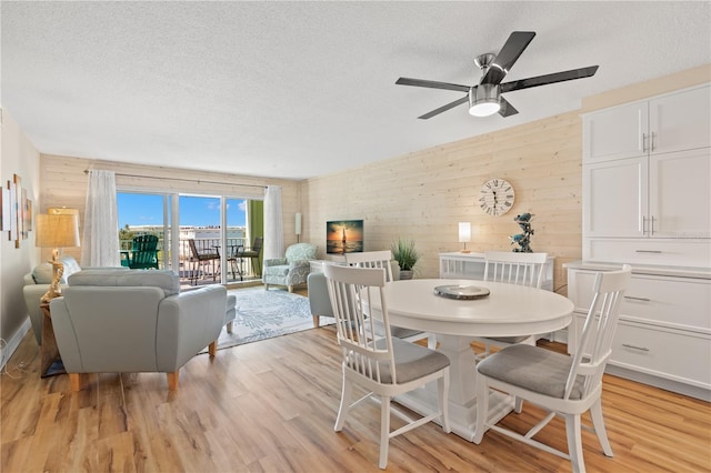 dining area featuring ceiling fan, wooden walls, a textured ceiling, and light wood-type flooring