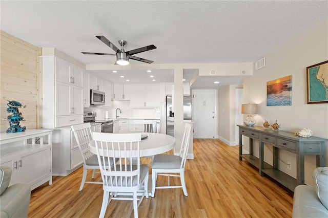 dining area featuring ceiling fan, sink, a textured ceiling, and light hardwood / wood-style floors