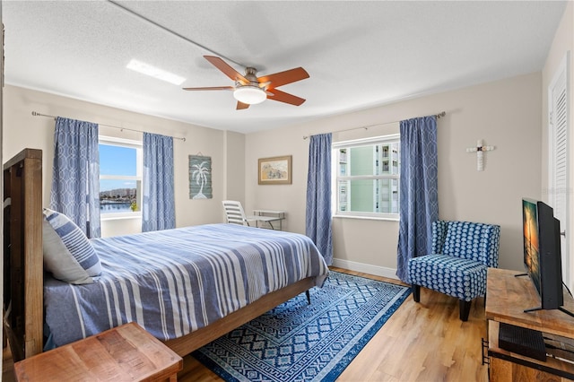 bedroom featuring multiple windows, ceiling fan, wood-type flooring, and a textured ceiling