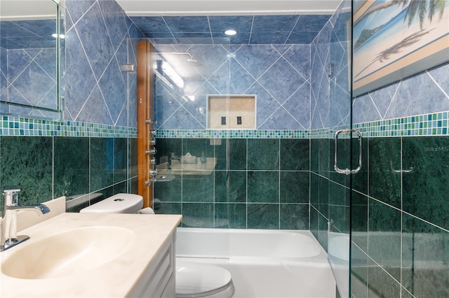 full bathroom featuring vanity, combined bath / shower with glass door, tile walls, and toilet