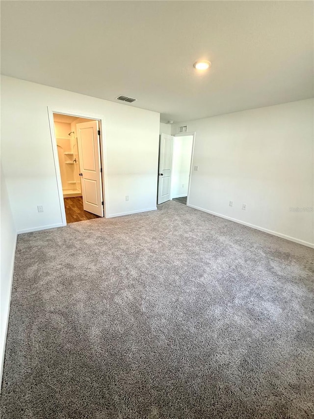 unfurnished bedroom with ensuite bath and dark colored carpet