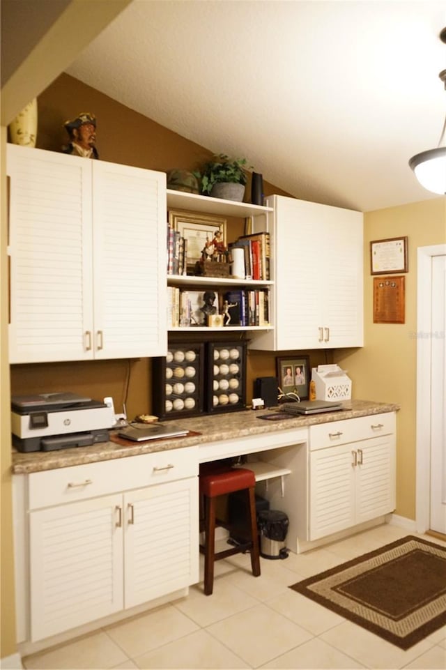 interior space featuring light tile patterned floors, vaulted ceiling, and white cabinets