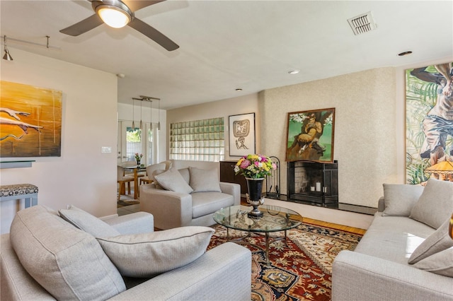 living room with visible vents, a fireplace with raised hearth, and a ceiling fan