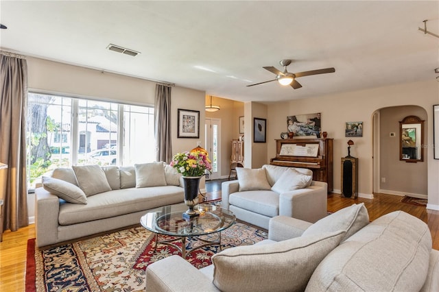 living room with baseboards, visible vents, arched walkways, ceiling fan, and light wood-style floors