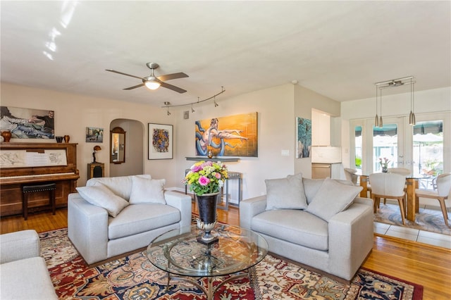 living area with arched walkways, wood finished floors, and a ceiling fan