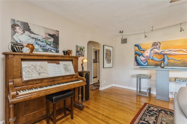 sitting room with arched walkways, visible vents, baseboards, and wood finished floors