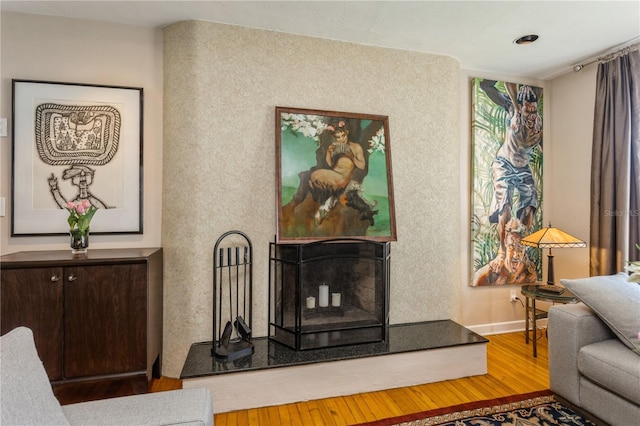 living area with a fireplace with raised hearth and wood finished floors