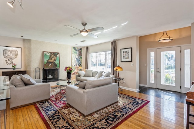 living area with visible vents, baseboards, a ceiling fan, a fireplace with raised hearth, and hardwood / wood-style floors