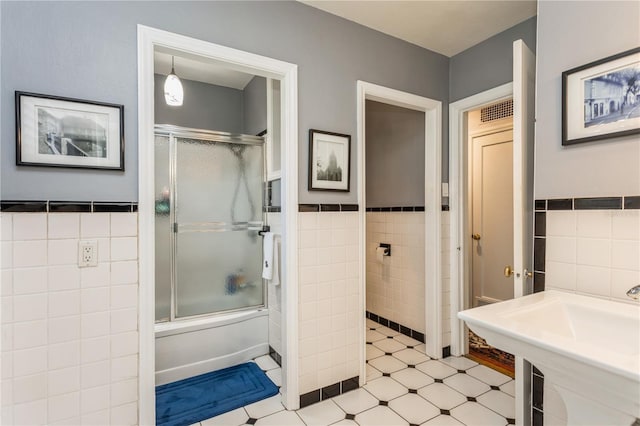 full bath with tile walls, bath / shower combo with glass door, wainscoting, a sink, and tile patterned floors