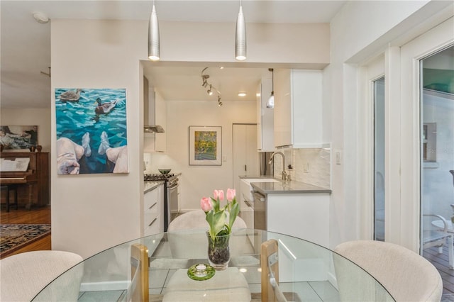 kitchen with decorative backsplash, appliances with stainless steel finishes, white cabinets, a sink, and wall chimney range hood